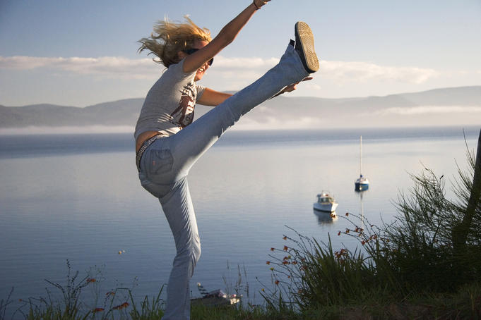Girl high-kicking with sea in background.