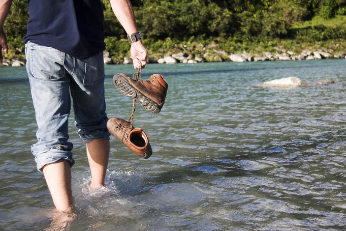 Hiker crossing stream with boots off.