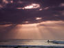 Lone surfer in sea with sunlight streaming through clouds.