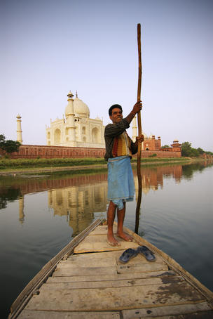 Boatman poling across Yamuna River beside Taj Mahal.