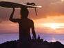 Surfer girl carrying surfboard silhouetted at sunset.