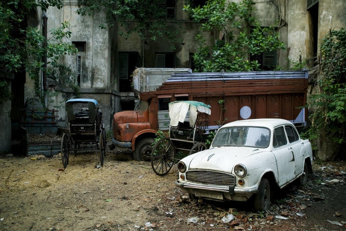 Rickshaws parked besides abandoned truck and car.