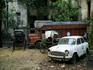 Rickshaws parked besides abandoned truck and car.