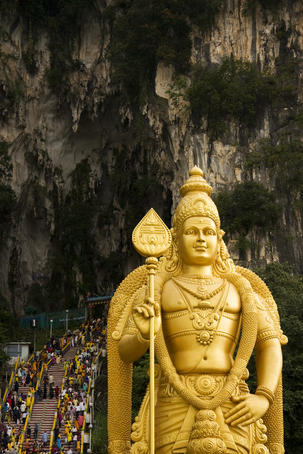 Crowd climbing steps to shrines in Batu Caves for the Thaipusam festival with Lord Muruga statue in foreground.