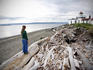 Woman standing on driftwood and looking towards Discovery Park Lighthouse.
