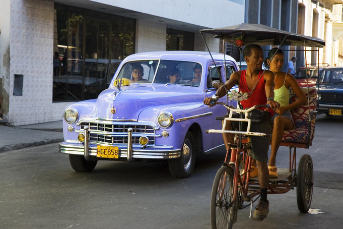 Taxi and cycle rickshaw travelling along street.