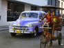 Taxi and cycle rickshaw travelling along street.