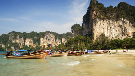 Limestone mountains and traditional longtail boats on beach.