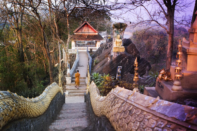 Monk walking down staircase framed by serpent bodies at one of many temples on the slopes of Phu Si.