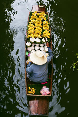 Fruit vendor on boat selling coconuts and bananas at Damnoen Saduak Floating Market.