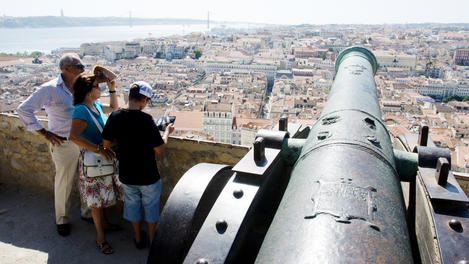Visitors looking over downtown panorama and River Tagus, from old cannon on walls of Castelo de Sao Jorge.