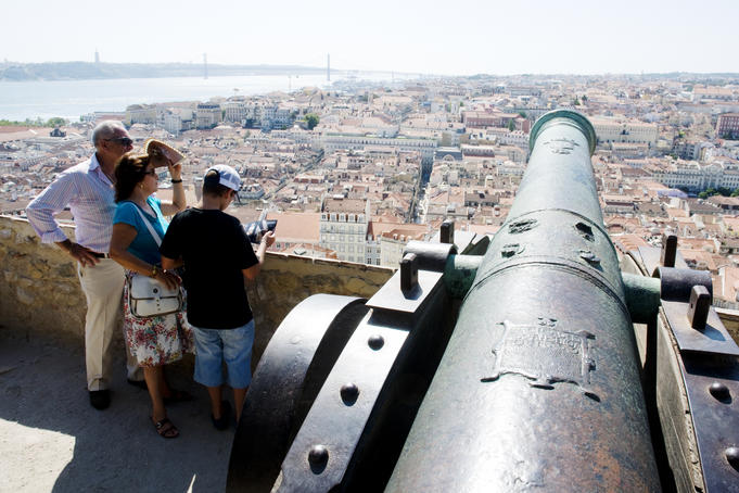 Visitors looking over downtown panorama and River Tagus, from old cannon on walls of Castelo de Sao Jorge.