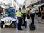 Mobile police unit comprising electric buggy and two-wheel "walking bikes" pause as passer-by takes photograph, Baixa (downtown) district.