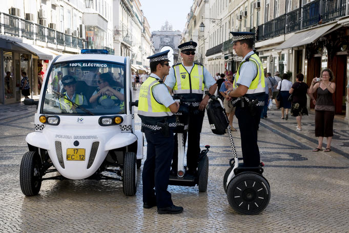 Mobile police unit comprising electric buggy and two-wheel "walking bikes" pause as passer-by takes photograph, Baixa (downtown) district.