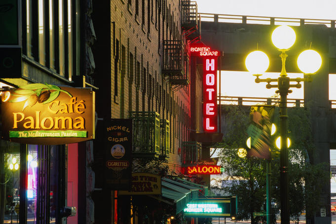 Cafe signs and others, lit up as dusk approaches on Yesler Way near Pioneer Square