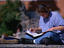 A student sitting cross-legged on a stone step, studying while listening to music through headphones, at the University of Arizona