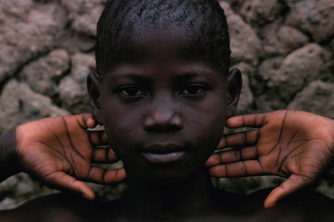 Portrait of a young boy with his hands by his head.