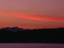 Looking across a body of water to the Olympic Mountain range, silhouetted against a soft red and pink sunset