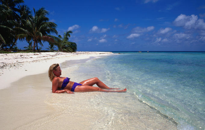 A woman sunbathing in the shallows on a sandy beach on one of the cayes off the coast of Belize