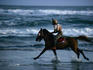 Boy riding pony on beach.
