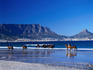 People riding racehorses on the beach at Bloubergstrand, with the city and Table Mountain in the distance