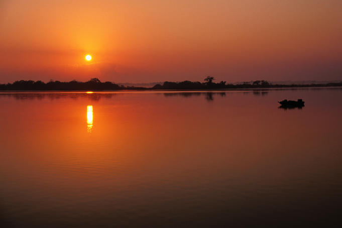 The sun rises over the peaceful waters of the New River at Lamanai Lagoon.