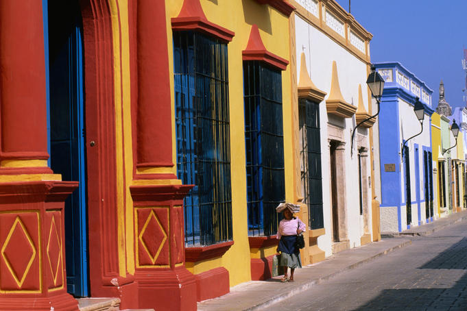 Woman walking past colourful house facades on street.