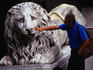 A tourist pokes a finger at a lion statue outside the Cathedral of San Lorenzo.