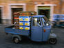 A swooping, fast paced, three wheel truck makes its way through the Campo de' Fiori Market in Rome