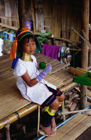 A young girl from the Longneck (Shan) village wearing the traditional Longneck jewellery sitting on the porch of a house