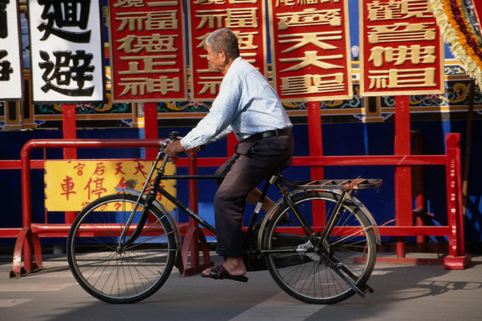 An older man on a bicycle in front of Chinese signs.