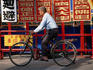 An older man on a bicycle in front of Chinese signs.