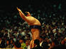 A Sumo wrestler performs his pre-bout stretching to the crowd at a packed stadium.