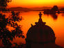 Silhouette of domed building on shore of Lake Pichola at sunset.