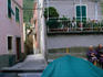 Elderly women chatting in the town square. A terraced vineyard typical of the Cinque Terre area can be seen beyond the square.