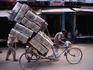 Rickshaw carrying load of metal containers.