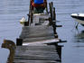 A lone angler sitting at the end of a rickety wooden jetty, fishing.