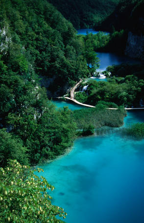 Wooden walkways arcing over the surface of azure pools at the base of steep forested mountains in the Plitvice National Park.