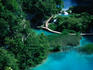 Wooden walkways arcing over the surface of azure pools at the base of steep forested mountains in the Plitvice National Park.