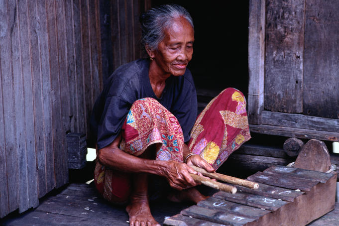 An elderly woman plays the xylophone on the verandah of her stilt house in Kampung Penambawan.