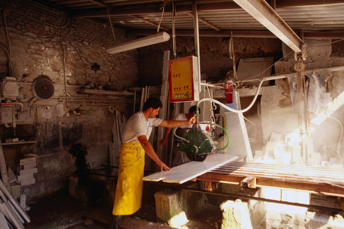 A worker slicing slabs of marble with a machine in a marble factory.