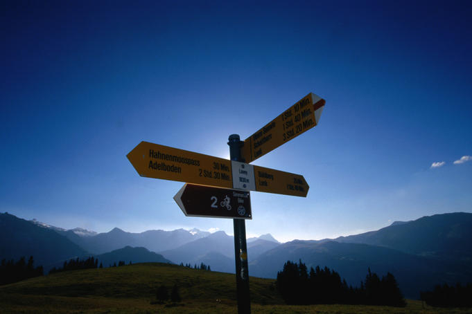 Hiking sign post near Hahnenmoospass with Bernese Alps in the background.