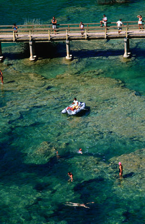 People swimming and boating near bridge on Krka River.