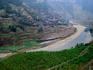 Aerial view of a village with surrounding pink fertilised rice fields cascading down rural mountains.