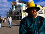 Man wearing beer stein hat and other people on boardwalk.