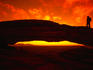 Silhouette of a hiker on Mesa Arch against a spectacular orange sky.