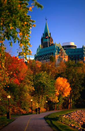 Autumn colours along path on Ottawa River bank, with Parliament building towering in the background