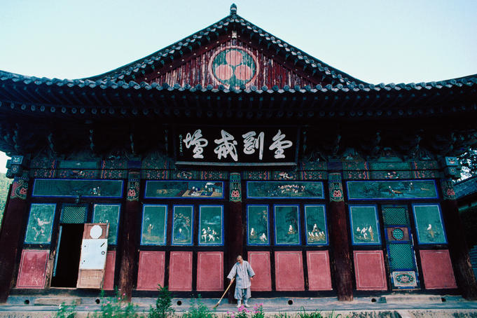 A monk sweeps outside the front entrance to a Buddhist temple.