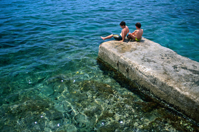 Two boys relax on a jetty surrounded by clear blue water, Cadaques