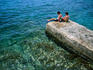 Two boys relax on a jetty surrounded by clear blue water, Cadaques